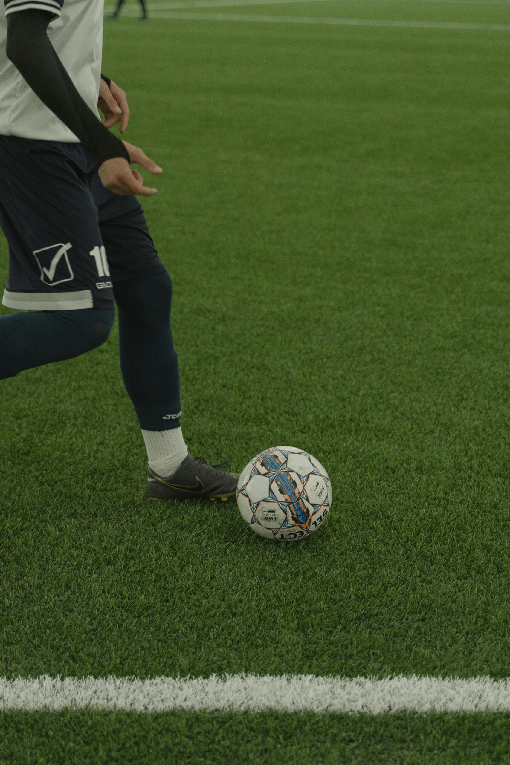 A soccer player dribbles a ball on a green field during a match, wearing a uniform.